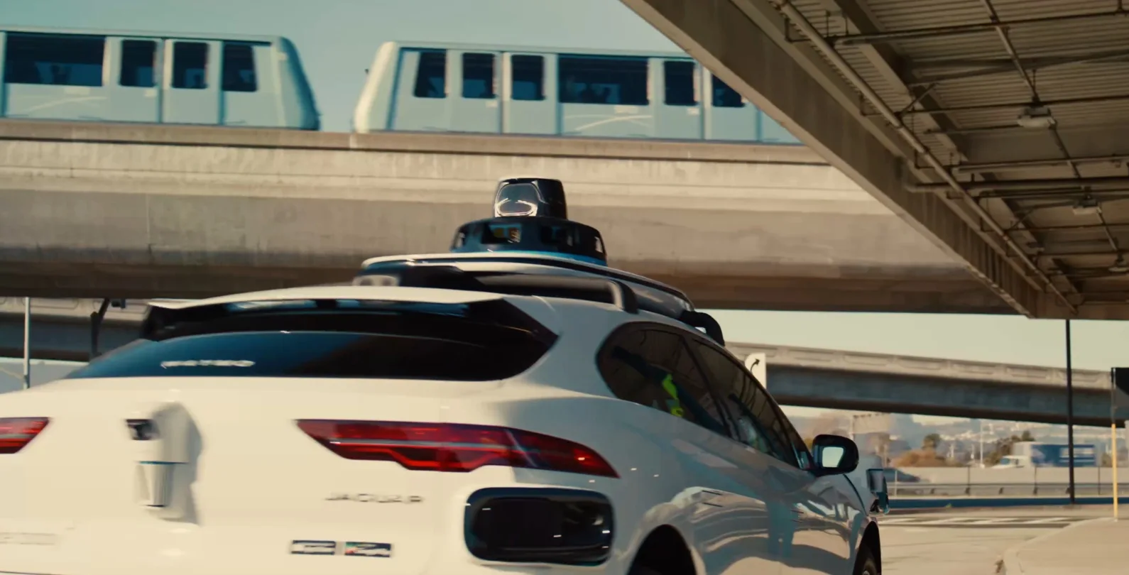 A Waymo vehicle at SFO, passing under an SFO AirTrain track.